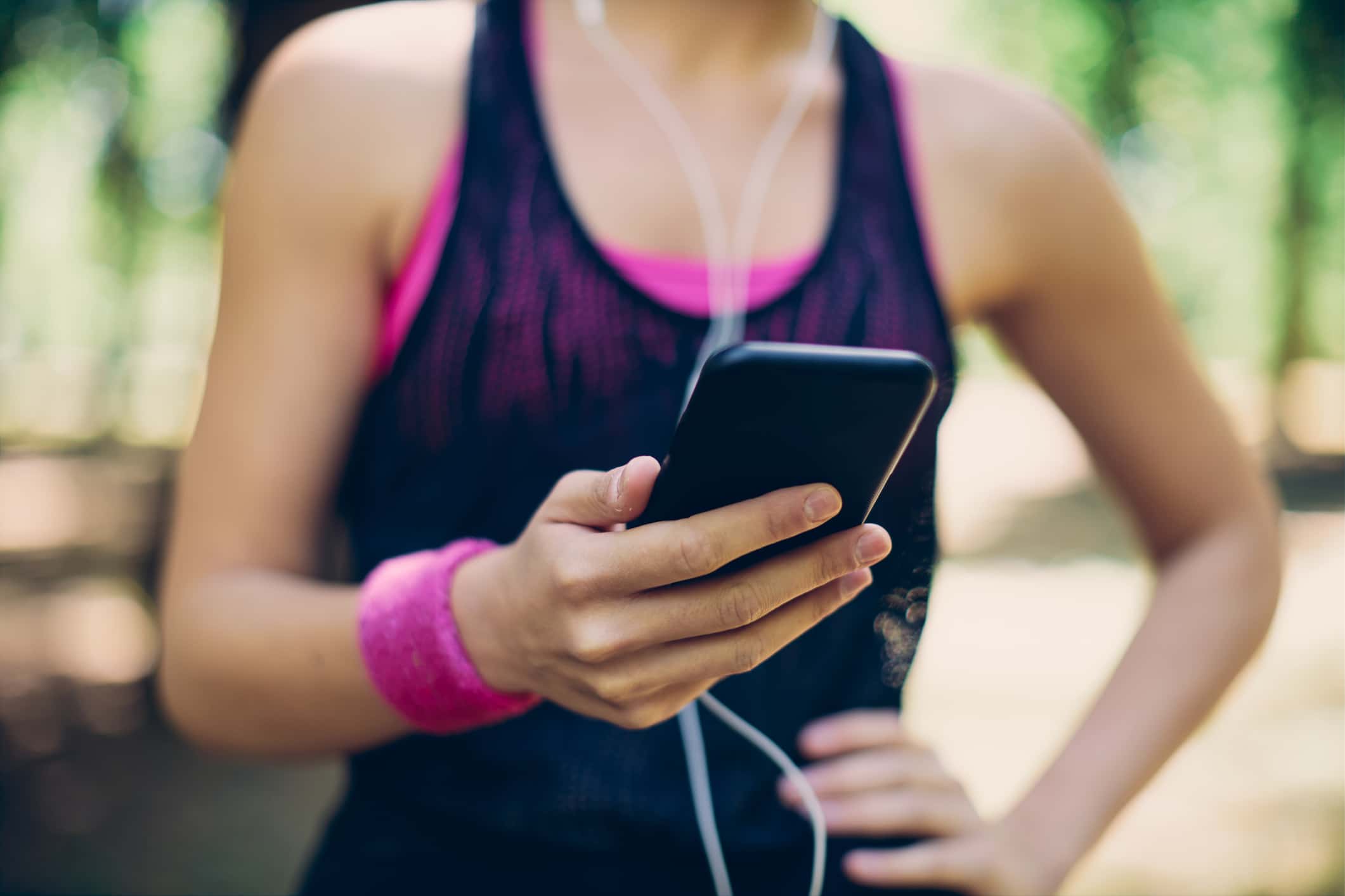 Closeup Of Attractive Caucasian Sportswoman Using Smart Phone While Standing In Nature On Beautiful Sunny Day.