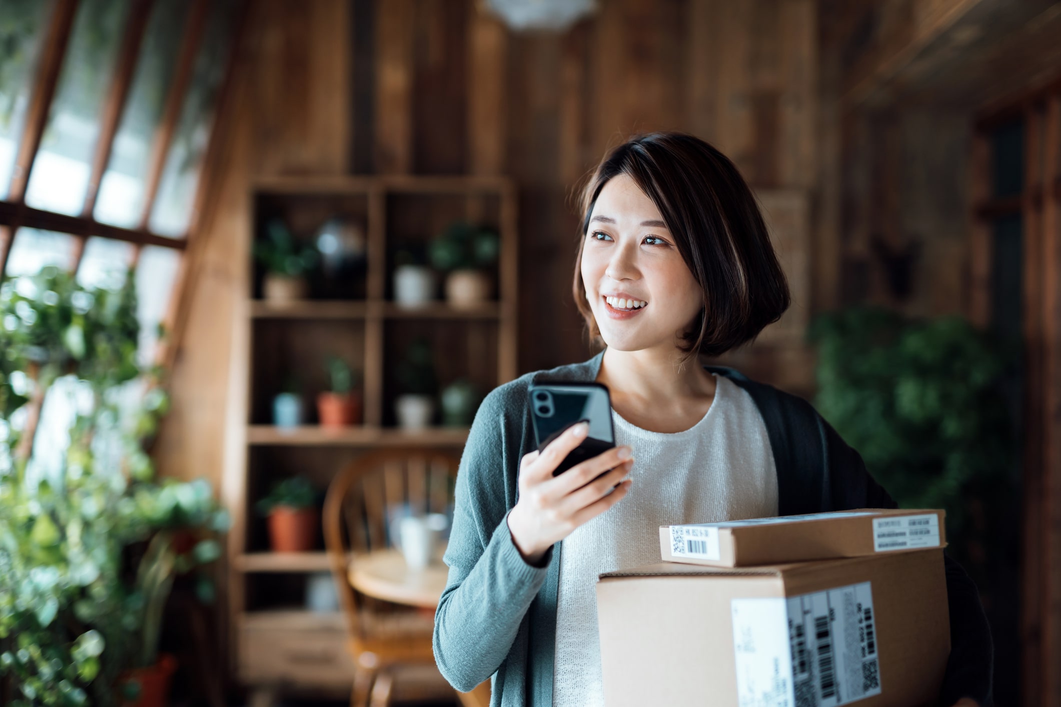 Beautiful Smiling Young Asian Woman Shopping Online With Smartphone And Receiving Parcels With Home Delivery Service. Express Online Shopping Online Banking. Enjoyable Shopping Experience