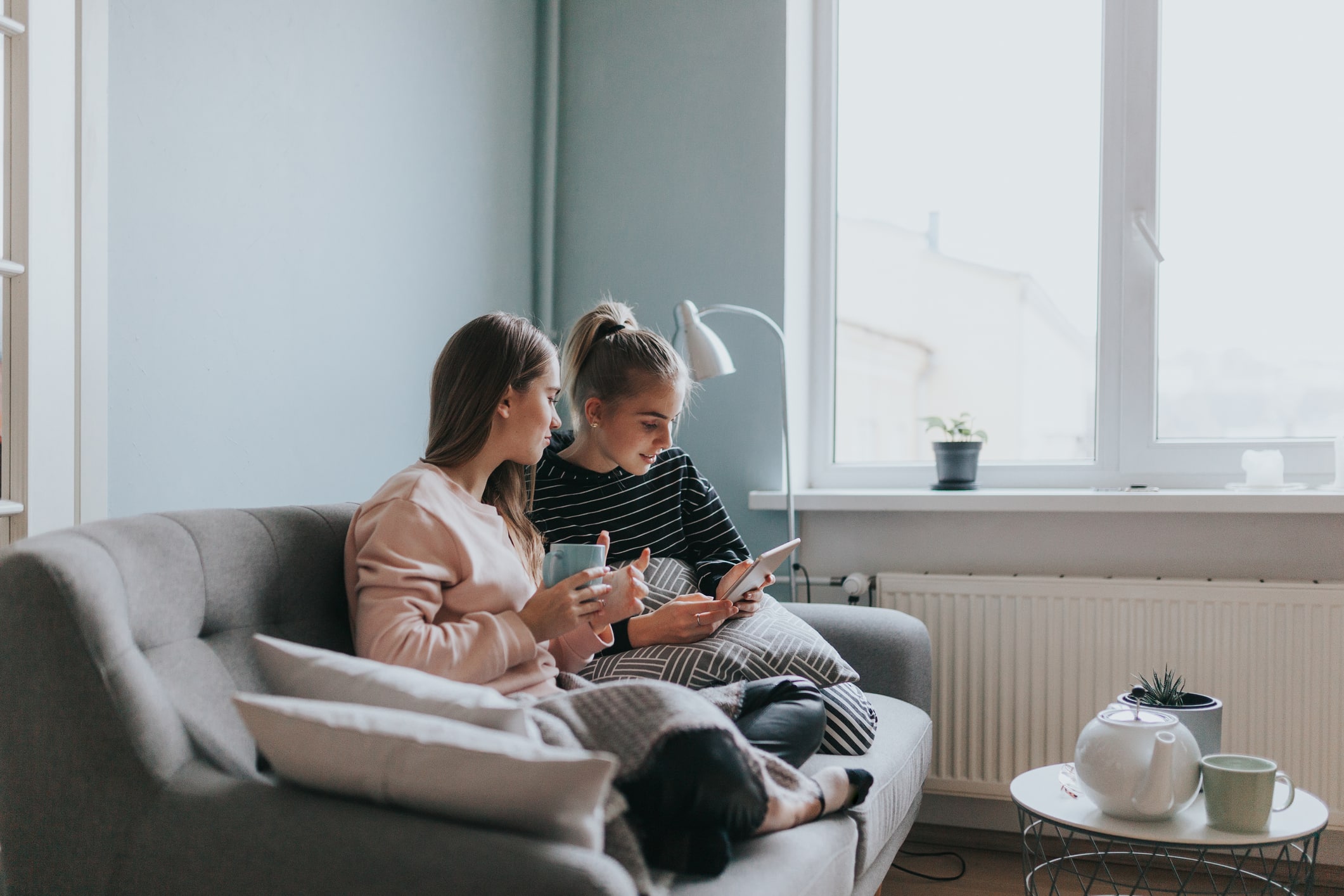 Two Teenage Girls Having A Video Call Conversation At Home On The Couch