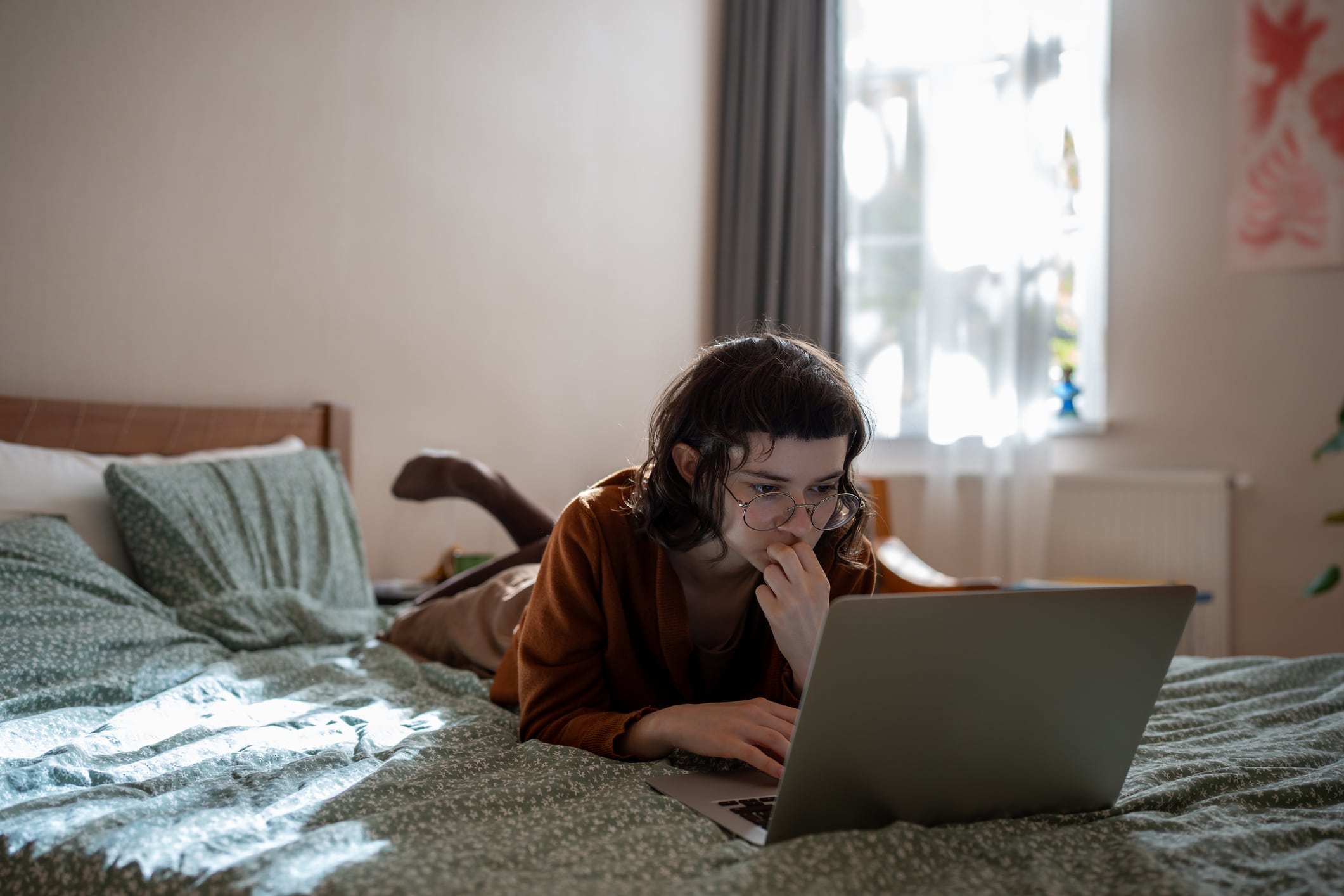 Student Girl Nerd In Glasses Studying On Laptop At Home Lying In Bed. Distant Education Homework